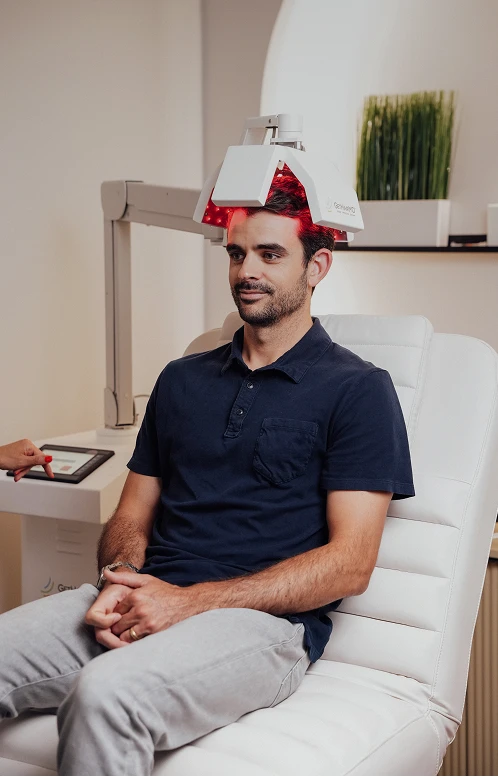 A patient undergoes clinical-grade low-level laser therapy (LLLT) using a stationary multi-panel red light device designed for hair stimulation.
