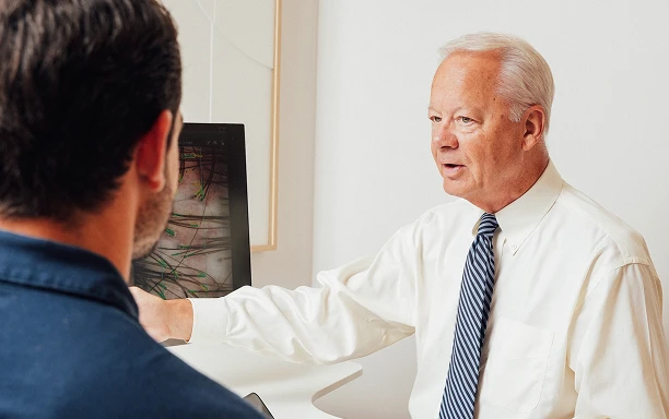 Dr. Carullo speaks with a male patient during an initial hair loss consultation in a bright office setting.