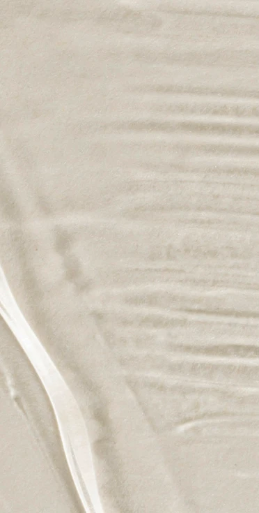 An abstract, high-key background texture featuring a smooth, milky white liquid surface with soft ripples and subtle shadows.