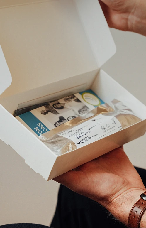 A close-up of a person's hands holding an open white Get Hair MD box containing instructional materials and treatment products.