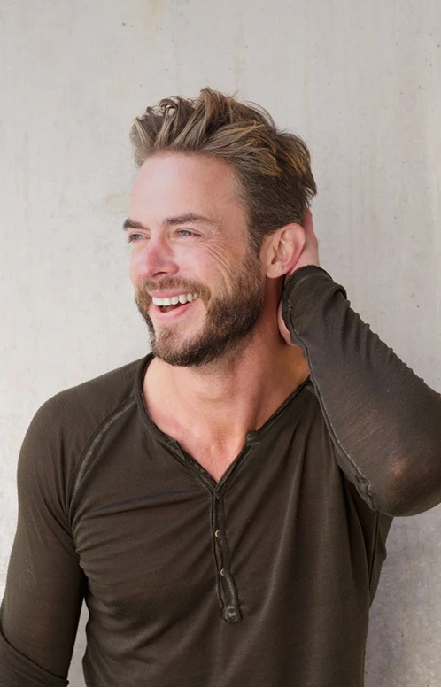 A smiling man with healthy, thick hair runs his hand through his hair, representing successful treatment results.