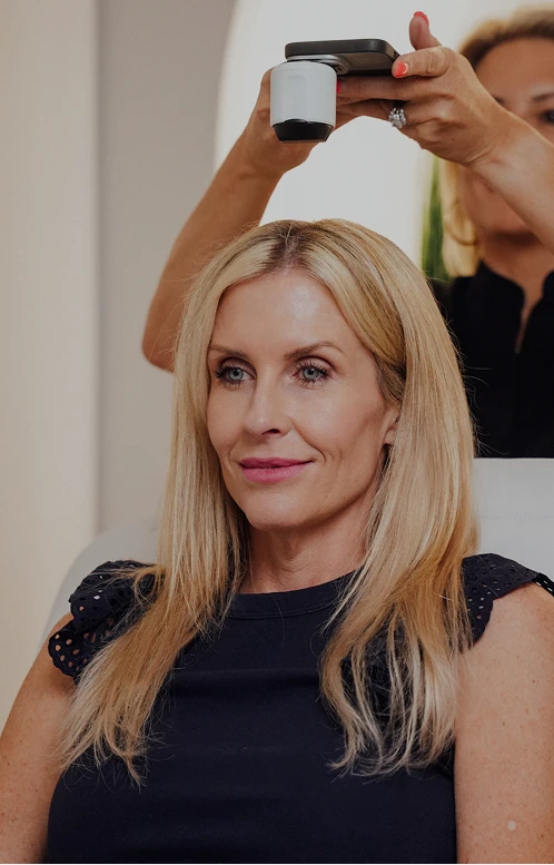 A patient at Get Hair MD sits comfortably while a clinician uses a specialized handheld device to perform a non-invasive scalp treatment.