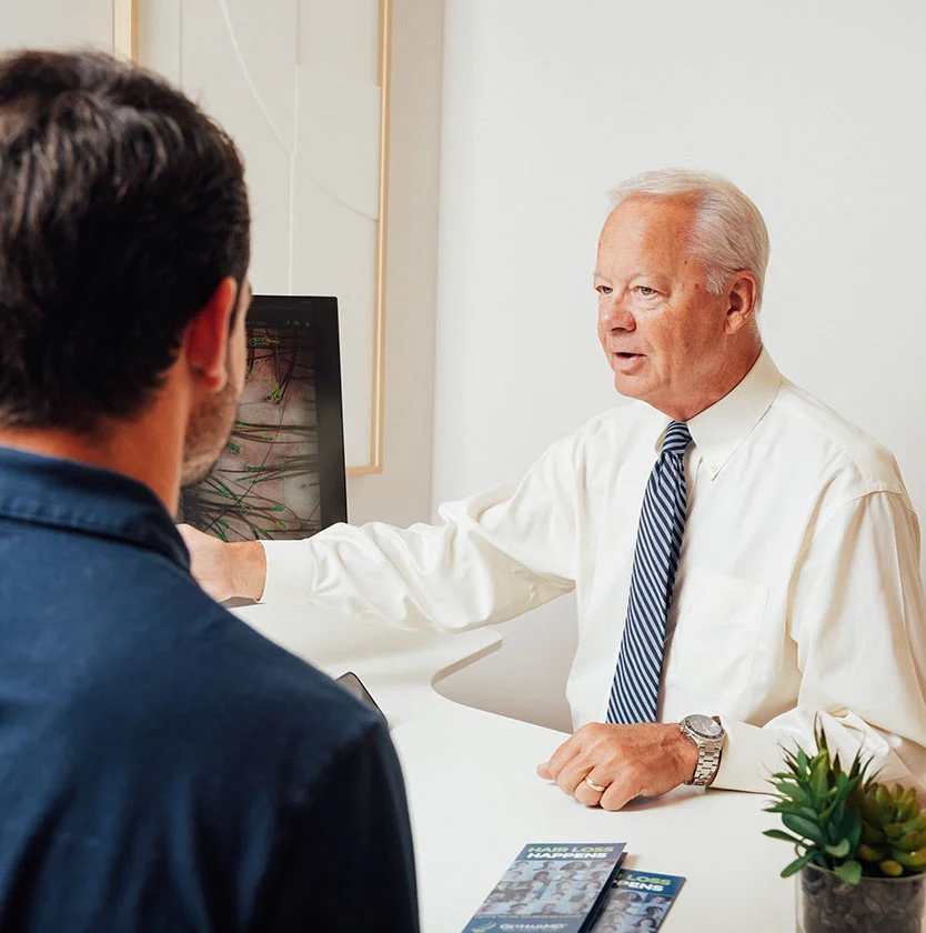 Dr. Keller speaks with a male patient during an initial hair loss consultation in a bright office setting.